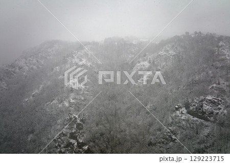 Aerial foggy landscape with mountain cliffs covered with fresh fallen snow during heavy snowfall in winter mountain forest on cold quiet day 129223715