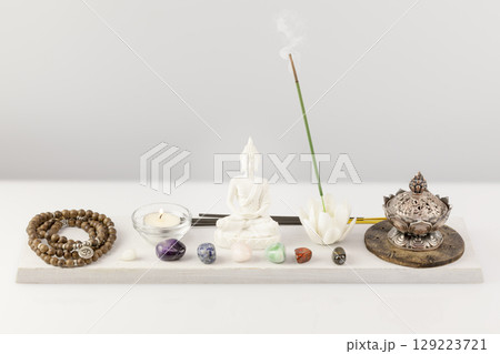 Self-care, healing composition with rosary beads, aroma bowl, aroma stick, buddha figurine, chakra stones and candle on white table. Concept of Me time, relaxing at home, energy healing and meditation 129223721