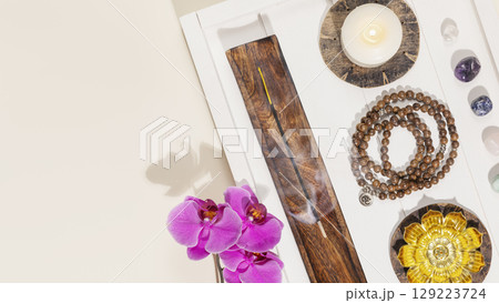 Self-care, healing banner with rosary beads, candles, aroma sticks, chakra stones and orchids on white wooden tray with copy space. Concept of me time, relaxing at home, energy healing and meditation 129223724
