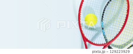 Tennis competition banner. Sport composition with yellow tennis ball and tennis rackets on a blue background with copy space.Tennis background. Sport and healthy lifestyle Tennis competition banner. Sport composition with yellow tennis ball and tennis rackets on a blue background with copy space.Tennis background. Sport and healthy lifestyle 129223929
