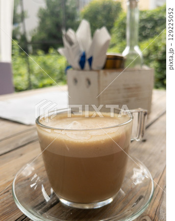 Glass cup of coffee on rustic wooden table in outdoor cafe 129225052