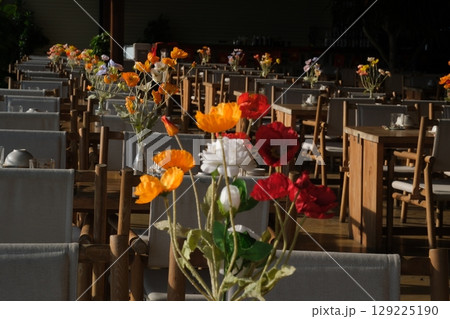 Cozy table setting with fall decor, flowers and utensils in dining room. Bouquet of fall flowers. Cozy kitchen interior. Festive table with wicker napkins, white plates and cutlery on wooden table. Cozy table setting with fall decor, flowers and utensils in dining room. Bouquet of fall flowers. Cozy kitchen interior. Festive table with wicker napkins, white plates and cutlery on wooden table. 129225190