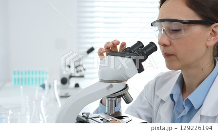 Female scientist examining samples through a microscope in a modern lab, conducting pharmaceutical research and developing treatments. Medicine, healthcare and science concept Female scientist examining samples through a microscope in a modern lab, conducting pharmaceutical research and developing treatments. Medicine, healthcare and science concept 129226194