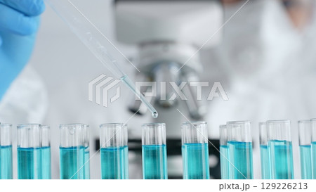 Close up of scientific researcher wearing protective gear, carefully pipetting liquid into test tubes while conducting medical research experiment in laboratory. Medicine, healthcare and science Close up of scientific researcher wearing protective gear, carefully pipetting liquid into test tubes while conducting medical research experiment in laboratory. Medicine, healthcare and science 129226213