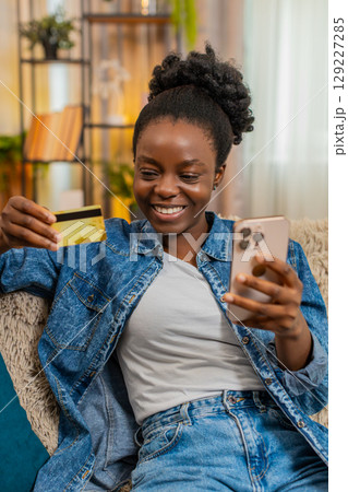 African American young woman shopping online on smartphone with credit card, smiling after purchase 129227285