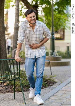 Indian young man traveler feeling sudden strong abdominal stomach ache, gastritis problem on street Indian young man traveler feeling sudden strong abdominal stomach ache, gastritis problem on street 129227572
