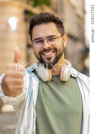Cheerful young Caucasian man showing double thumbs up gives positive reply standing on city street Cheerful young Caucasian man showing double thumbs up gives positive reply standing on city street 129227581