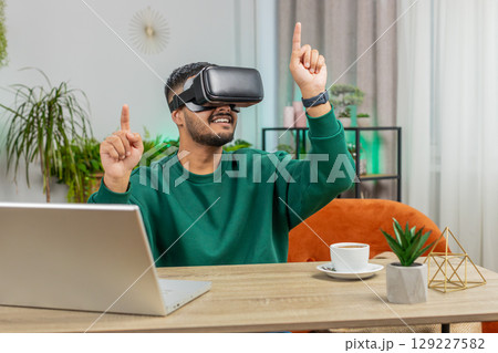 Indian man using virtual reality futuristic technology headset play simulation 3D video game at home 129227582