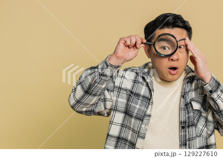 Asian mature man holds magnifying glass near face looking at camera with big zoomed eye, analyzing Asian mature man holds magnifying glass near face looking at camera with big zoomed eye, analyzing 129227610