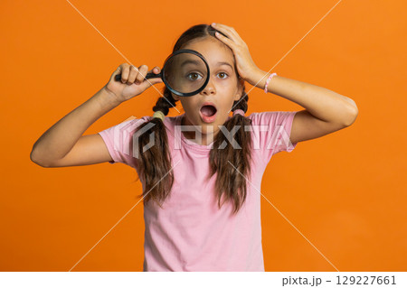 Child girl kid holds magnifying glass near face looking at camera with big zoomed eye, analyzing 129227661