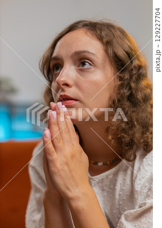 Sad woman sitting on sofa at home in shock by awful news, folding palms together pray ask for help Sad woman sitting on sofa at home in shock by awful news, folding palms together pray ask for help 129227704