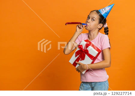 Happy excited lucky girl wearing birthday hat cone blow pipe celebrating party success win victory Happy excited lucky girl wearing birthday hat cone blow pipe celebrating party success win victory 129227714