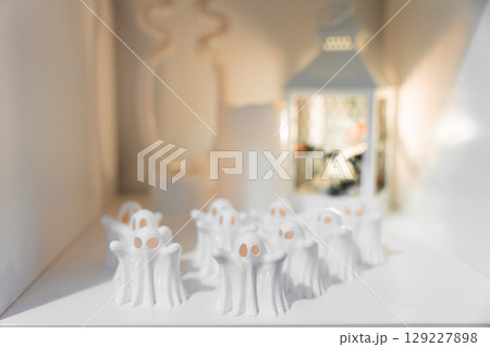 Mini white ghost figurines for Halloween decor on white background with warm lantern light. 129227898