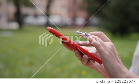 A woman engages with her smartphone while enjoying a summer day outdoors. The setting features green grass and a clear sky, creating a pleasant atmosphere for teamwork. A woman engages with her smartphone while enjoying a summer day outdoors. The setting features green grass and a clear sky, creating a pleasant atmosphere for teamwork. 129228077