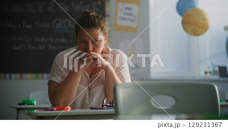 Tired Female Teacher Sitting Alone at the Desk in Empty Classroom, Relaxing After Class 129231367