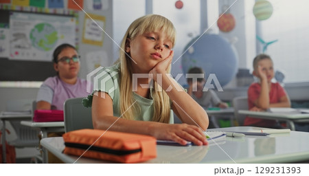 Sad Primary School Girl Sitting at Desk, Getting Tired During Lesson or Upset Because of Bad Grade 129231393