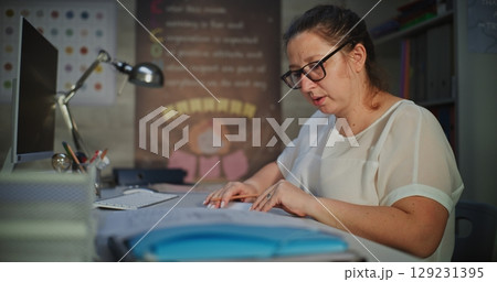 Female Teacher Sitting at Desk, Checking Homework of Students, Grading School Tests After Class 129231395