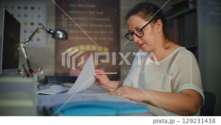 Female Teacher Sitting at Desk, Checking Homework of Students, Grading School Tests After Class 129231438