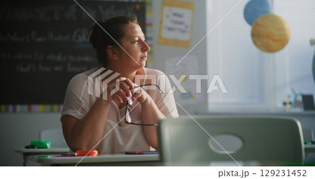 Tired Female Teacher Sitting Alone at the Desk in Empty Classroom, Relaxing After Class Tired Female Teacher Sitting Alone at the Desk in Empty Classroom, Relaxing After Class 129231452