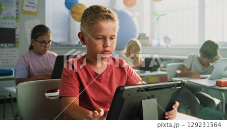 Elementary School Boy Sitting at Desk, Using Digital Tablet, Studying Basic Programming 129231564