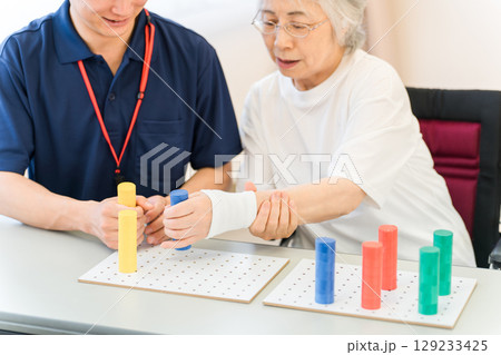 介護施設・リハビリ施設で働く作業療法士の職員とリハビリをするシニア女性 129233425