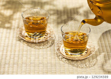 畳の上でやかんから麦茶をグラスに注ぐ和の涼を感じる夏 129234389