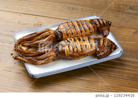 焼き色が香ばしい姿焼きのイカを皿に盛り付けた和風料理 129234416