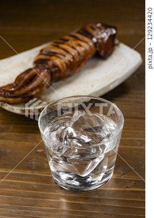 皿に盛られた姿焼きのイカと冷たい焼酎グラス 129234420