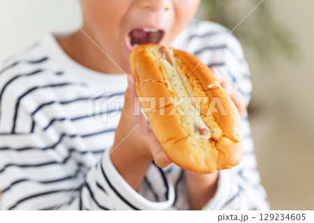 惣菜パンのホットドックを食べる小学生の男の子 129234605