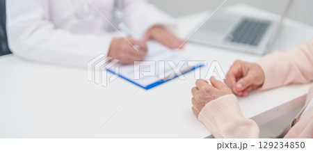 senior woman consulting with doctor in hospital. Elderly patient talking and sharing disease. Doctor listens, asking question and taking note. medical consultation and geriatric Healthcare concept 129234850