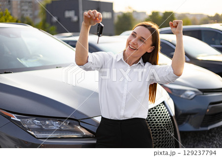 A happy woman celebrates the purchase of her new car, holding up the keys with joy at a dealership. 129237794