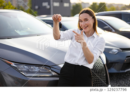 A smiling woman shows off the car keys after purchasing a new car. 129237796