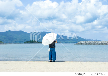＜素材＞夏の海の砂浜で遠くを見つめる女性 129237927