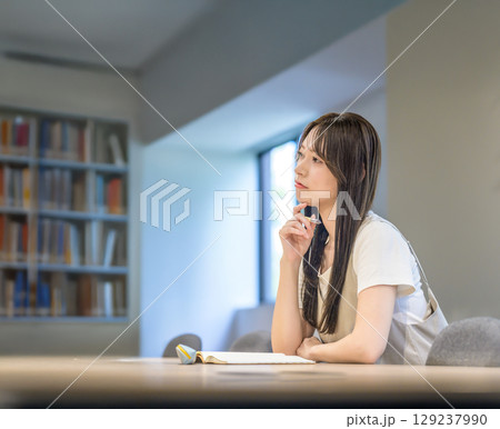 　本棚の前で考え事をする女子大学生 129237990