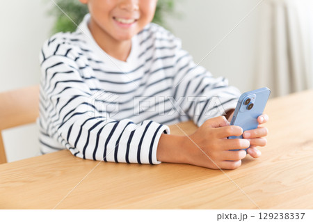 家でスマホを持って笑う小学生の男の子 129238337