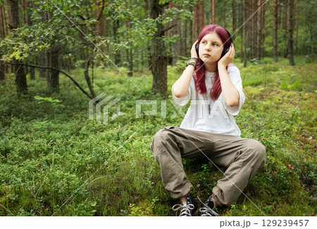 Young girl listening music with headphones in forest Young girl listening music with headphones in forest 129239457