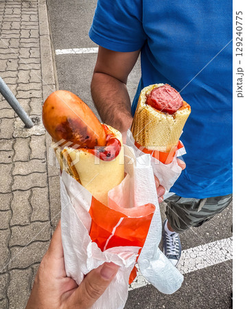 Street food hot dogs in baguette-style buns, held in hands. Outdoor casual meal. High quality photo Street food hot dogs in baguette-style buns, held in hands. Outdoor casual meal. High quality photo 129240775