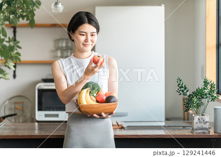 キッチンの前で野菜を持つスポーツウェア姿の若いアジア人女性(野菜不足・栄養バランス・緑黄色野菜) キッチンの前で野菜を持つスポーツウェア姿の若いアジア人女性(野菜不足・栄養バランス・緑黄色野菜) 129241446