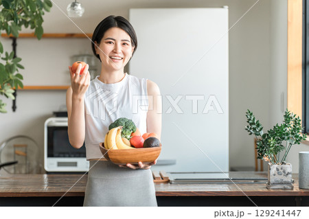 キッチンの前で野菜を持つスポーツウェア姿の若いアジア人女性（野菜不足・栄養バランス・緑黄色野菜） 129241447