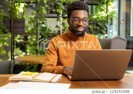 Young male entrepreneur in glasses doing online research using laptop in office 129242086