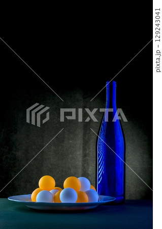 Still life with blue bottle and balls against a dark background 129243041