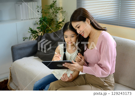 Smiling mother and daughter using digital tablet together at home 129243173