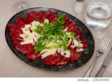 Raw veal meat carpaccio with cheese and fresh arugula 129243440