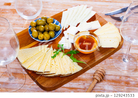 On wooden table there is cutting board with assorted cheese, honey, pickled olives - On wooden table there is cutting board with assorted cheese, honey, pickled olives - 129243533