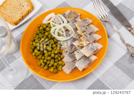 Pieces of herring served with green peas and onions. Appetizer fish on table 129243787