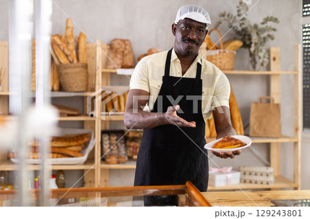 Joyful man baker presenting just baked pastry 129243801