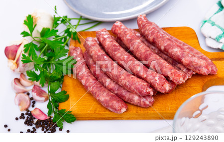 Raw sausages longaniza with greens, garlic and spices on wooden cutting board Raw sausages longaniza with greens, garlic and spices on wooden cutting board 129243890