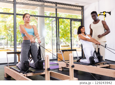 Two women having pilates workout on reformers with trainer Two women having pilates workout on reformers with trainer 129243942