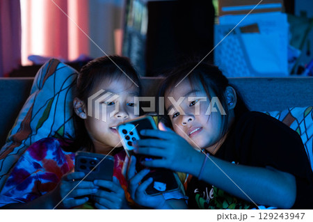 Two Asian child lying in bed using smartphone at night, screen light illuminating face, concept of screen time and digital addiction in kids Two Asian child lying in bed using smartphone at night, screen light illuminating face, concept of screen time and digital addiction in kids 129243947