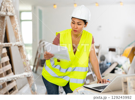 Woman engineer checking documents and using laptop during repair works 129243992
